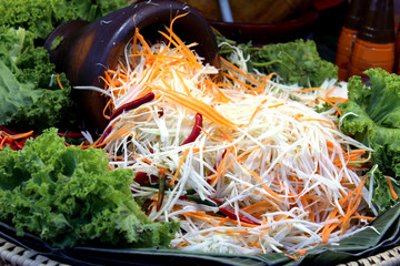 Shredded papaya and carrot slices with red chilli placed in front of the mortar to prepare thai...