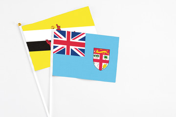 Fototapeta premium Fiji and Brunei stick flags on white background. High quality fabric, miniature national flag. Peaceful global concept.White floor for copy space.