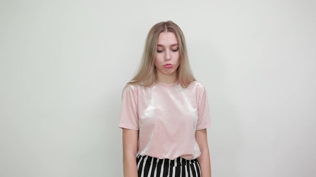 Surprised cheerful young woman in casual paspel pink shirt looking camera, showing tongue on white background in studio. People sincere emotions, lifestyle concept.