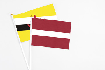 Latvia and Brunei stick flags on white background. High quality fabric, miniature national flag. Peaceful global concept.White floor for copy space.