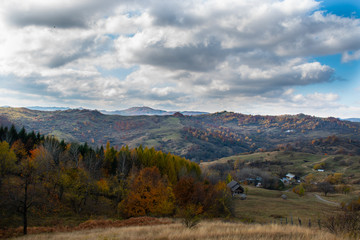 Beautiful sky and clouds over a forest on top of a hill near a small village, with autumn colored trees and autumn colors