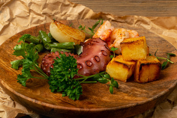 Grilled octopus tentacle on a wooden plate served with shrimps