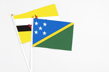 Solomon Islands and Brunei stick flags on white background. High quality fabric, miniature national flag. Peaceful global concept.White floor for copy space.