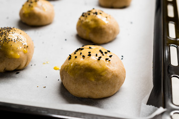 Cooking Raw Homemade Turkish Pastries Pogaca with Black Cumin and Sesame Seeds on Oven Tray with Baking Paper Sheet Ready to Bake and Oiling Pastry Bush.