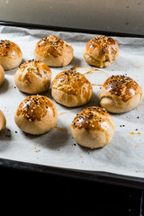Homemade Turkish Pastries Pogaca with Black Cumin and Sesame Seeds on Baking Paper Sheet with Tray.