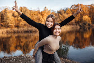 Carefree two young twin sisters in casual outfit with bright smile showing peace gesture at the park. Freedom concept.