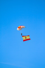 Paratrooper with the open paraglider and a large flag of Spain held in flight with a nice blue background and a helicopter