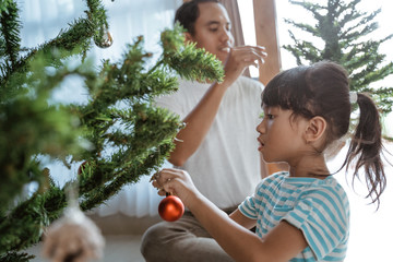 asian father and daughter installing newly bought artificial christmas tree at home