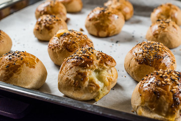 Homemade Turkish Pastries Pogaca with Black Cumin and Sesame Seeds on Baking Paper Sheet with Tray.