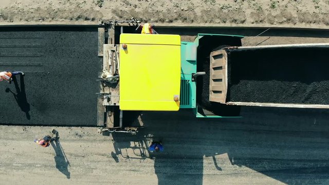 Road workers are laying bitum on the fresh road. Asphalt paver machine on a road construction site.