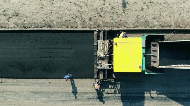 Asphalt paver machine on a road construction site. Road makers are throwing bitum from the machinery