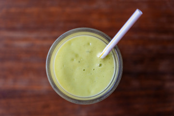 Glass of avocado smoothie with drinking straw on wooden background, top view