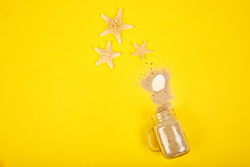 Starfishes and seashells, glass with sand on yellow background