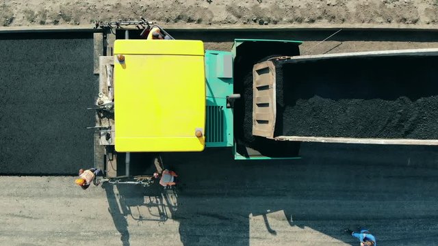 Asphalt paver machine on a road construction site. Top view of trucks filled with bitum and workers around them
