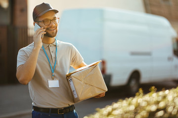 Young happy delivery man talking on the phone while carrying packages.
