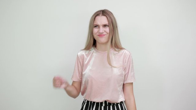 Caucasian attractive girl over white wall making unimportant gesture while lifting the shoulders wearing pastel pink shirt