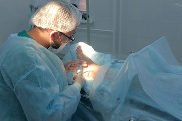 Surgeon man sutures ankle during surgery with neat stitches after removing hygroma. Doctor sewing...