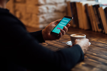 Man holds mobile phone with internet banking and coffee cup