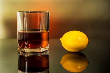 glass of whiskey with lemon on a table with reflection