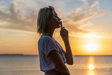 Silhouette of woman holding finger on her lips against a beautiful sunset near sea waves on the...