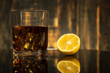 glass of whiskey with lemon on a table with reflection