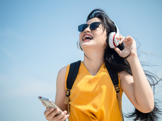 Happy Asian woman with backpack using headphone on the beach, lifestyle concept.