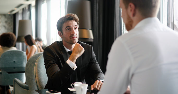 Image of young businessman with cup of coffee communicating with colleague