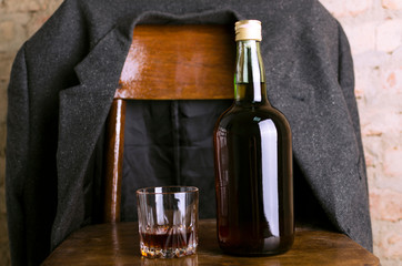 Bottle of rum and old-fashioned glass on the retro wooden chair, male coat on it