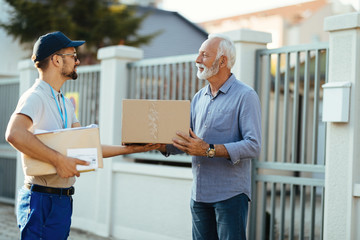 Senior man receiving packages from a deliverer in front of his house.