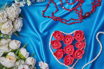 Heart of red flower buds on a blue beautiful fabric with beads of pearls and coral top view
