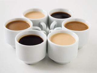 Several mugs with different coffee lined up in a circle on a white background. White coffee set