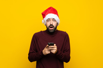 Man with christmas hat over isolated yellow background surprised and sending a message