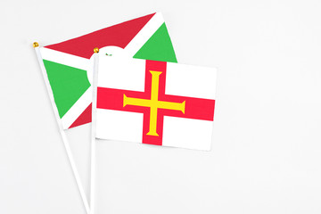 Fototapeta premium Guernsey and Burundi stick flags on white background. High quality fabric, miniature national flag. Peaceful global concept.White floor for copy space.