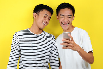 Portrait of happy two casual men smiling look at smartphone. Portrait of handsome two young men looking at their phone and smiling