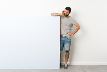 Young handsome man with beard holding a big blue empty placard with headache