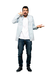 Fototapeta premium Full-length shot of Handsome man with beard making phone gesture and doubting over isolated white background