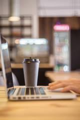 Brown paper cup of coffee, place for text logo, laptop freelancer hand, bokeh background.