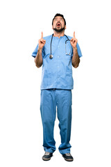 Full-length shot of Surgeon doctor man surprised and pointing up over isolated white background