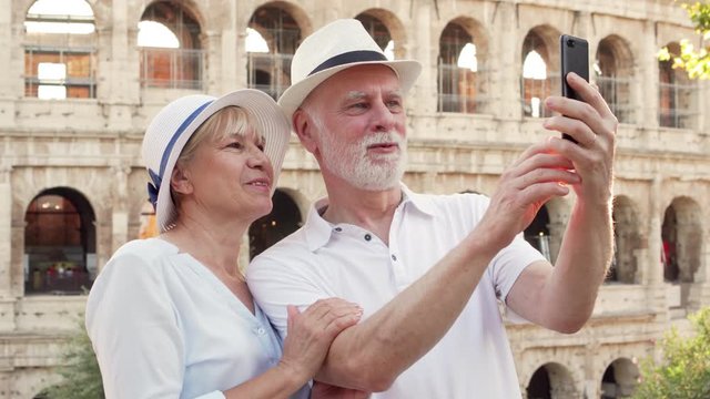 Happy tourists family in hats enjoy vacation in Rome. Senior couple take selfie with cellphone near famous Italian attraction Colosseum. Having fun travelling together