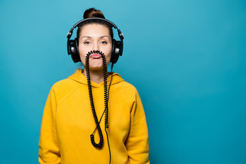 The girl in the big headphones is fooling around, holding the wire between her lip and nose