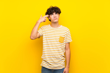 Young man over isolated yellow wall with problems making suicide gesture