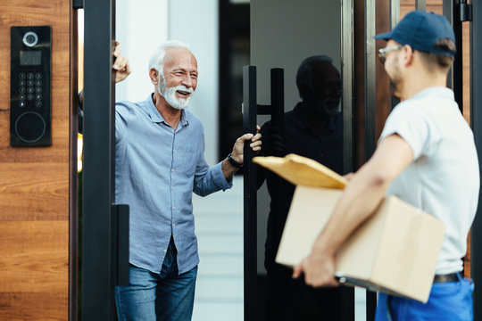 Happy Senior Man Opening Door To The Delivery Man.