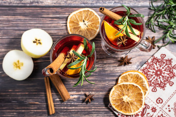 Flat lay overhead of two glasses of hot spicy mulled wine on dark wooden table fruits, herbs, spices and traditional decor.
