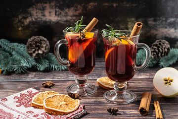 Two glasses of hot traditional Christmas drink mulled wine or grog with spices, herbs and fruits on dark rustic background with festive decor.  Christmas and New Year concept.