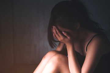 Naklejka premium Sad depressed woman suffering from family life. women sitting in dark room cryng, palm close her face. Young beautiful women thinking how to solve problem.