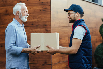 Young smiling courier delivering package to a senior customer.