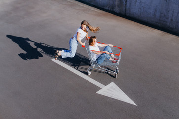 Two happy hipster girls having fun with shopping cart outdoors