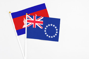 Fototapeta premium Cook Islands and Cambodia stick flags on white background. High quality fabric, miniature national flag. Peaceful global concept.White floor for copy space.