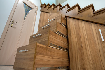 Modern architecture interior with luxury hallway with glossy wooden stairs in multi-storey house. Custom built pullout cabinets on glides in slots under stairs. Use of space for storage.
