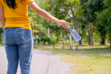 Yellow t-shirt woman is throwing plastic bottle on the road of garden or park.
